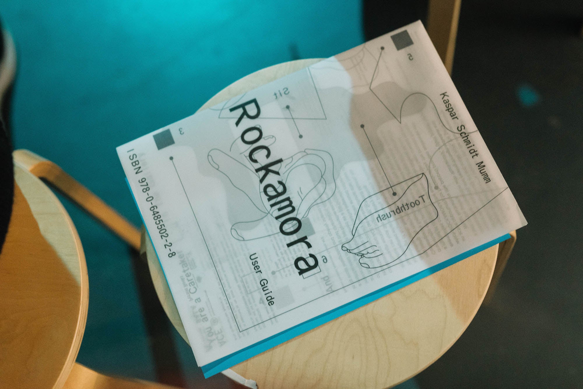A photograph of the ROCKAMORA catalogue sitting on atop a stool in the gallery.